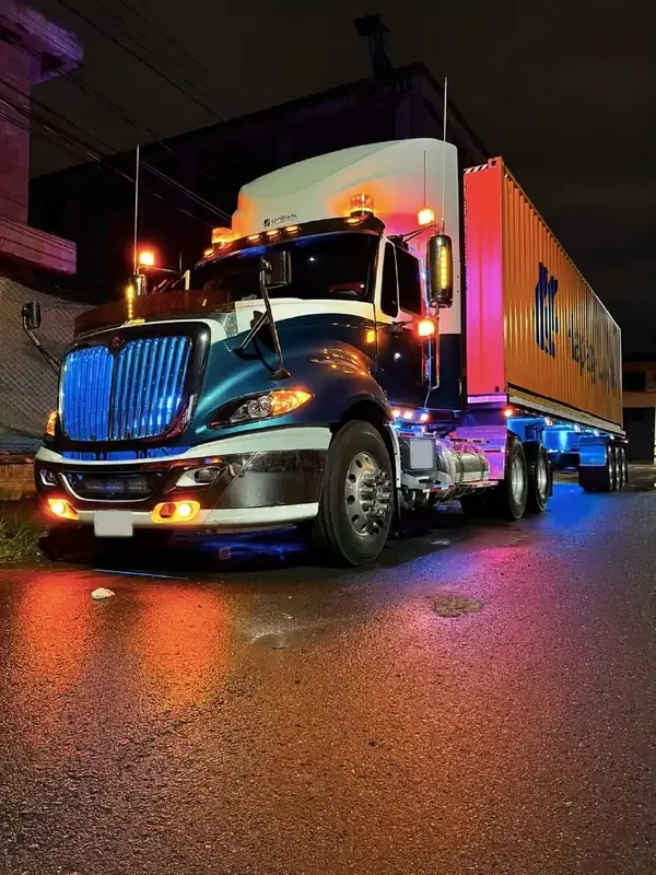 Tractocamión de Caritrans con contenedor, de noche y con las luces encendidas